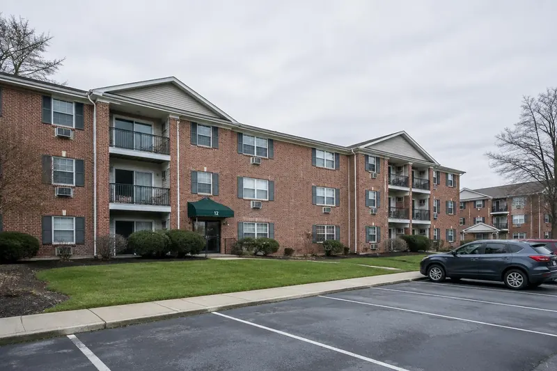 Three-story brick garden-style apartment complex with a front lawn and parking area